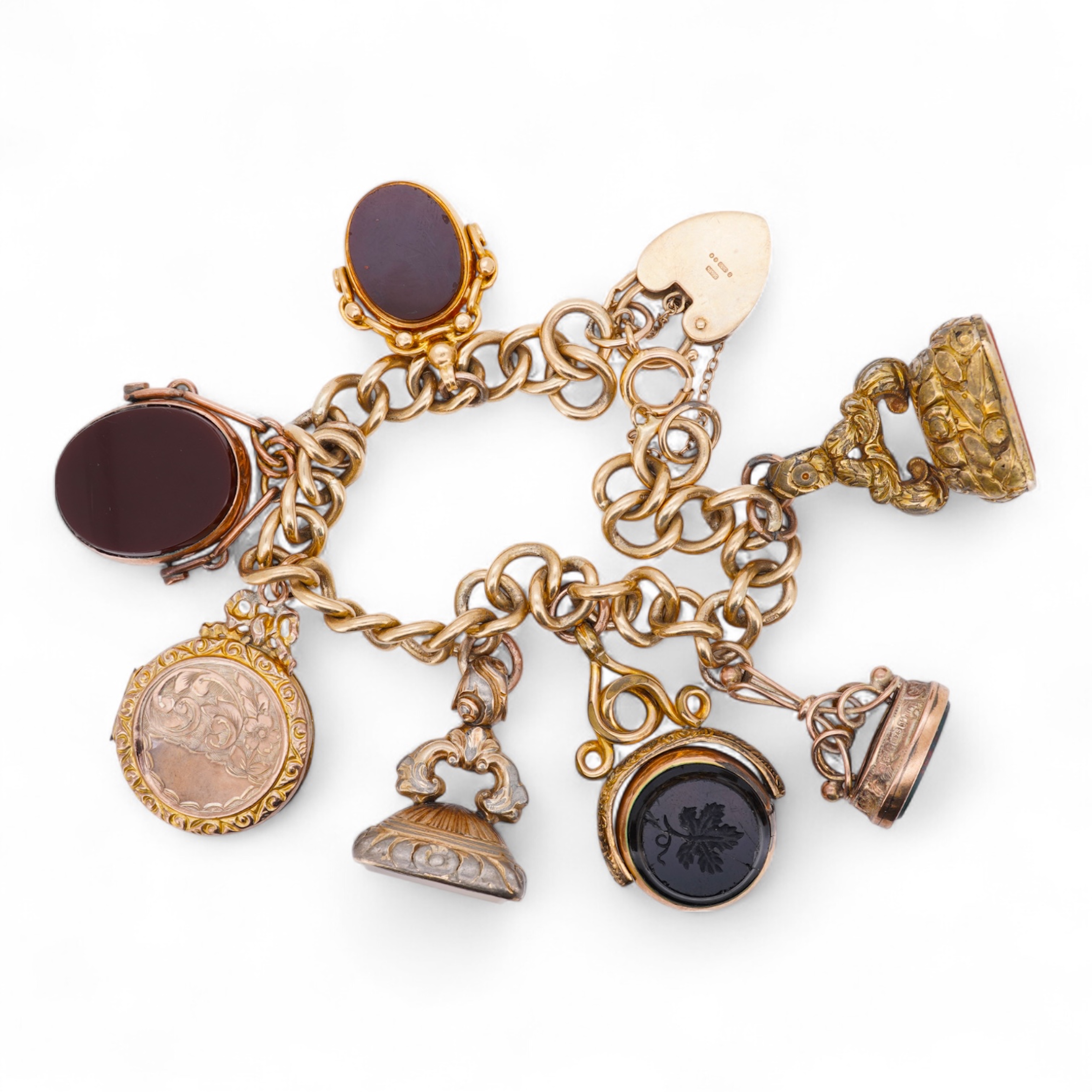 A 1970's 9ct gold curb link charm bracelet, with 9ct gold heart shaped clasp, hung with seven assorted gold or gilt metal mounted charms including six chalcedony set fob seals, gross weight 73 grams.